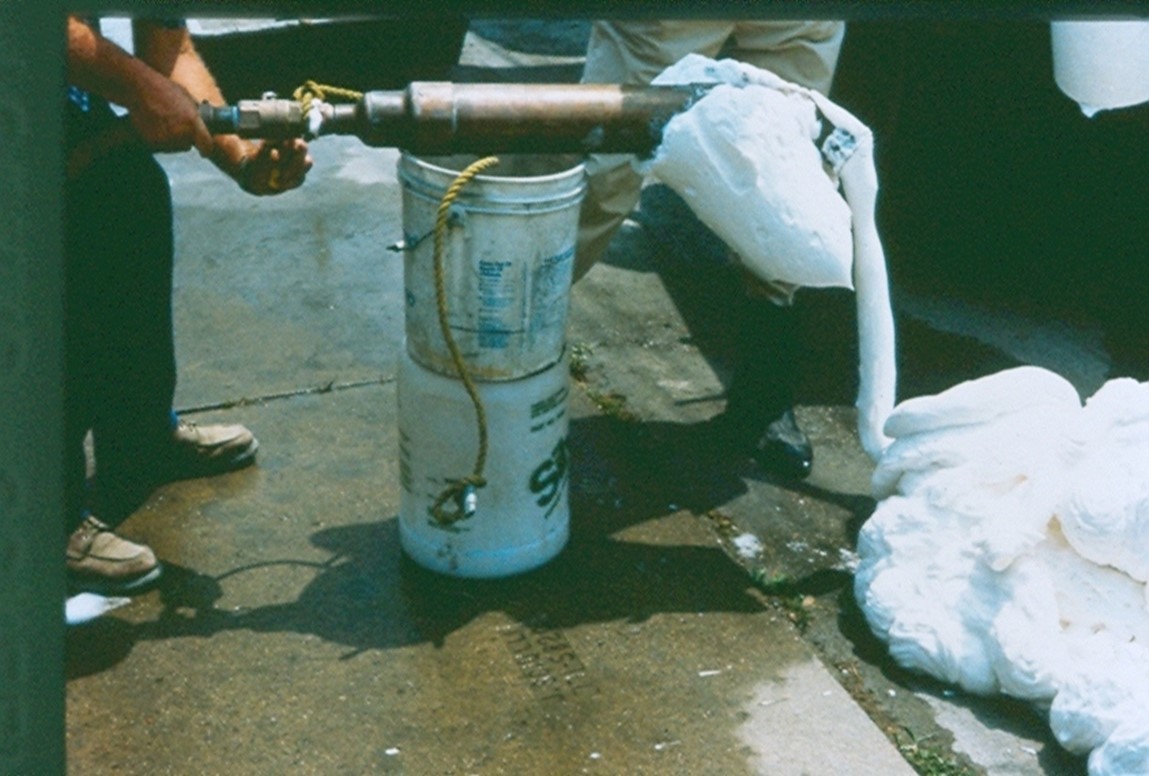 A photo by Greg Hensley, shows a piece of equipment which can dig a trench 3 feet by 10 feet to a predetermined depth.  There are two large cutting wheels attached to a crane-like tracked equipment.  The image shows workers cleaning the cutting heads after completing a vertical trench cut.