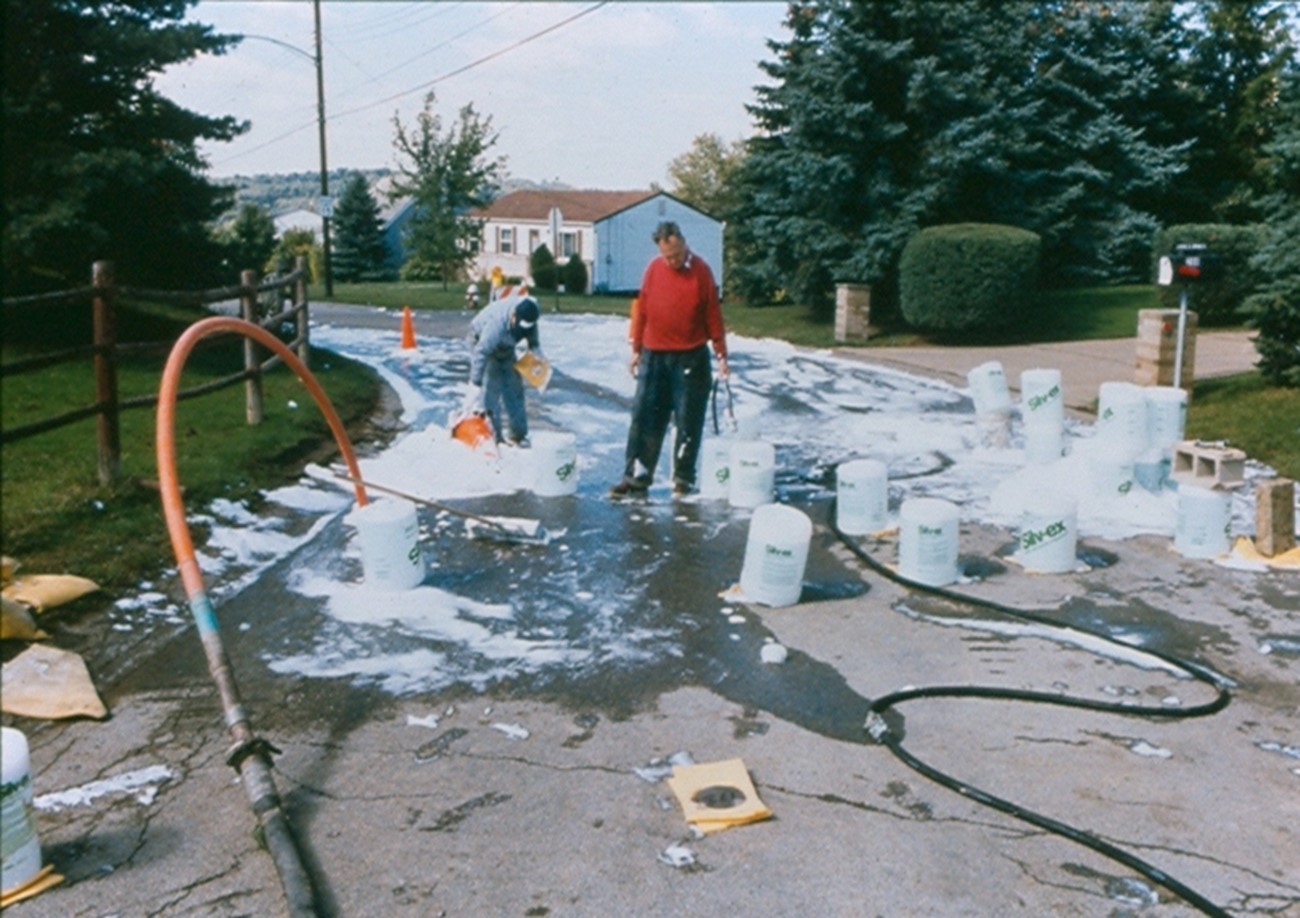 This image shown workers injecting foam into a mine fire.  The hoses show where the foam is being injected and the containers of foam are strewn around as they are emptied and injected. 