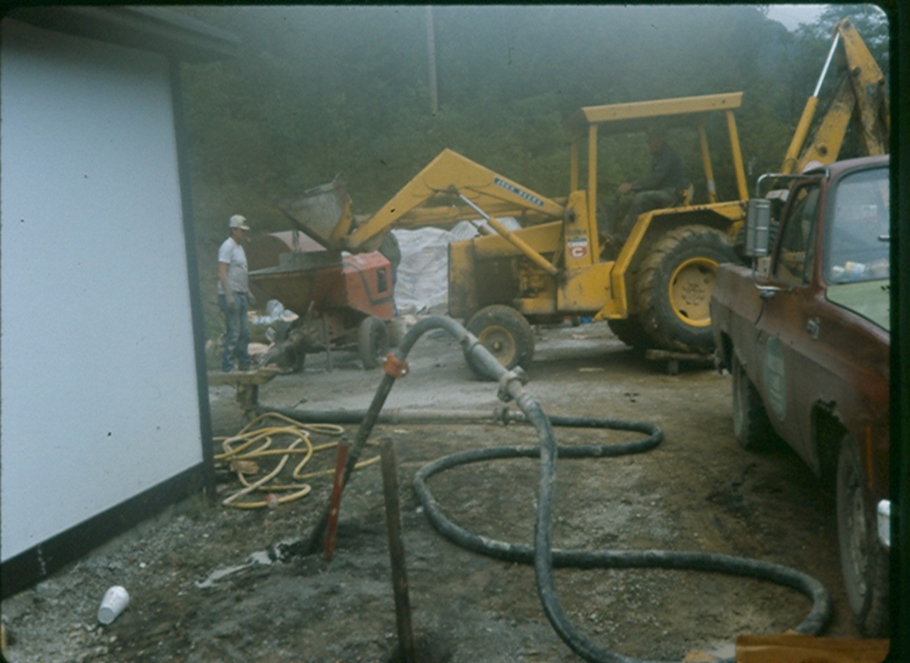 This image shows grout being injected to prevent an occupied structure from being affected by coal mine gob pile fires.  The image shows a backhoe adding grout to a grout pump which then injects it into the ground at a predetermined level. 