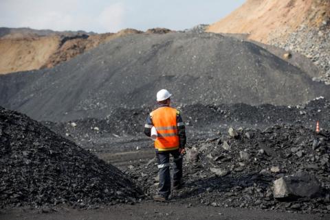 A man in a hard hat and bright orange safety jacket surveys an active coal mine site.