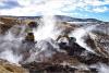 Heavy equipment works along a brown hilly landscape surrounded by rolling smoke.